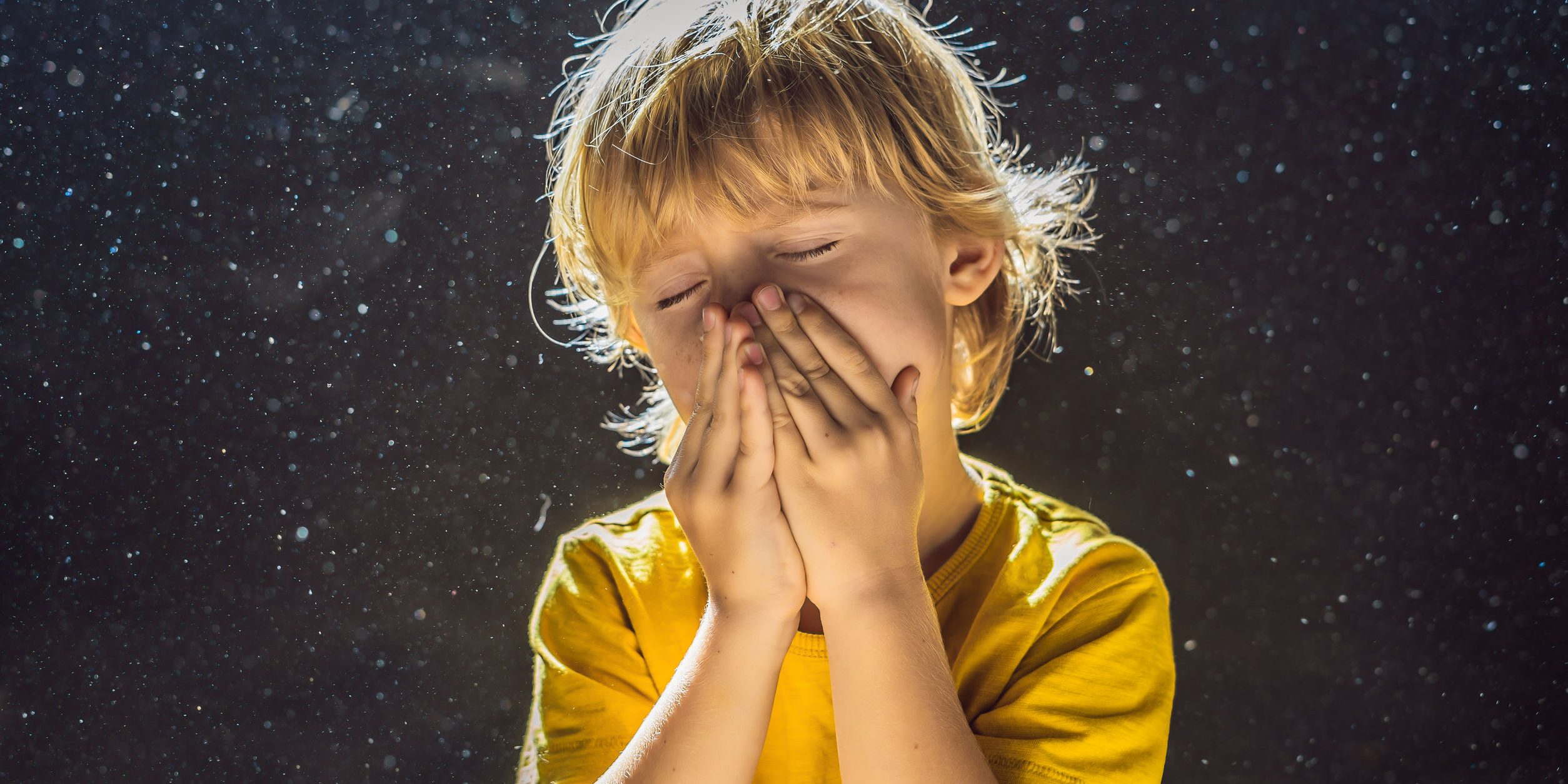 Allergy to dust.Boy sneezes because he is allergic to dust. Dust flies in the air backlit by light.