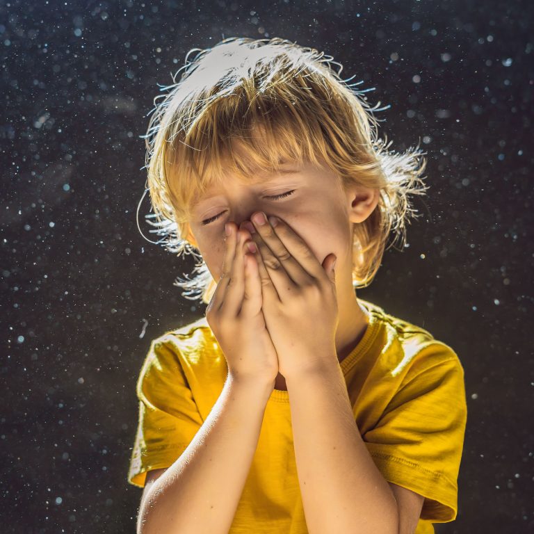 Allergy to dust.Boy sneezes because he is allergic to dust. Dust flies in the air backlit by light.