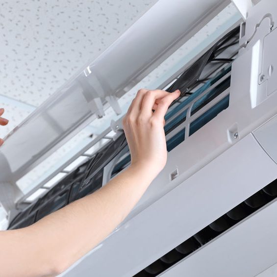 Young woman cleaning air conditioner, indoors