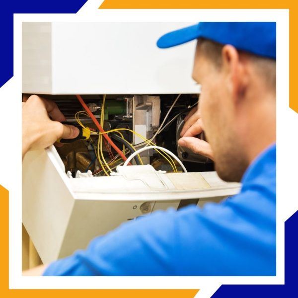 Heating Installation Greeley 1 A technician in a blue cap works on the internal wiring and components of a furnace.