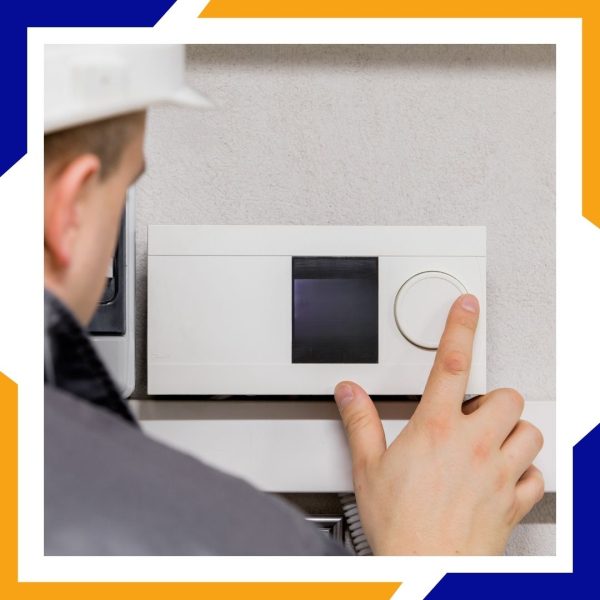 Heating Installation Loveland 3 A technician in a hard hat adjusts the dial on a large, modern wall-mounted climate control unit.