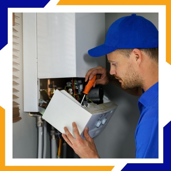 A focused technician in a blue cap uses a screwdriver to service a wall-mounted boiler unit.