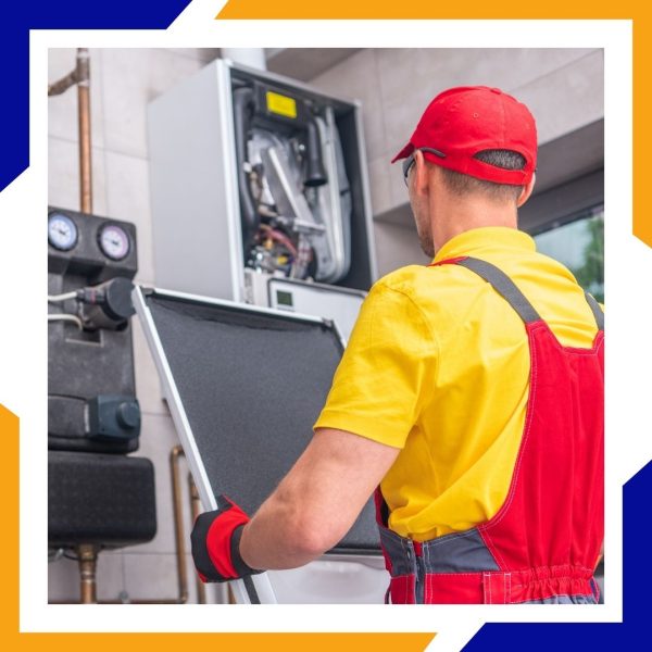 A technician in red overalls removes the front cover from a complex boiler and heating system.