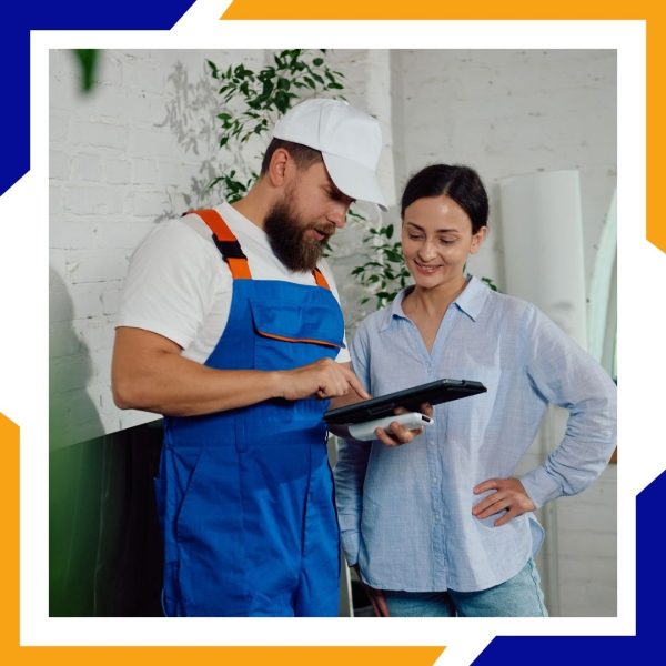 A male HVAC technician in a white cap shows a female homeowner information on a digital tablet.